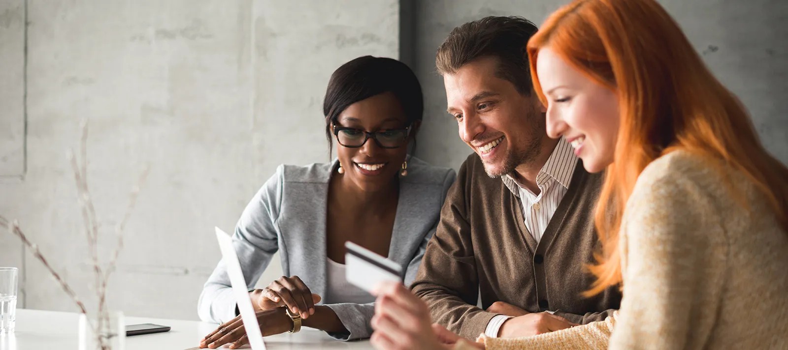 group of business professionals gathered around a laptop screen holding a credit card