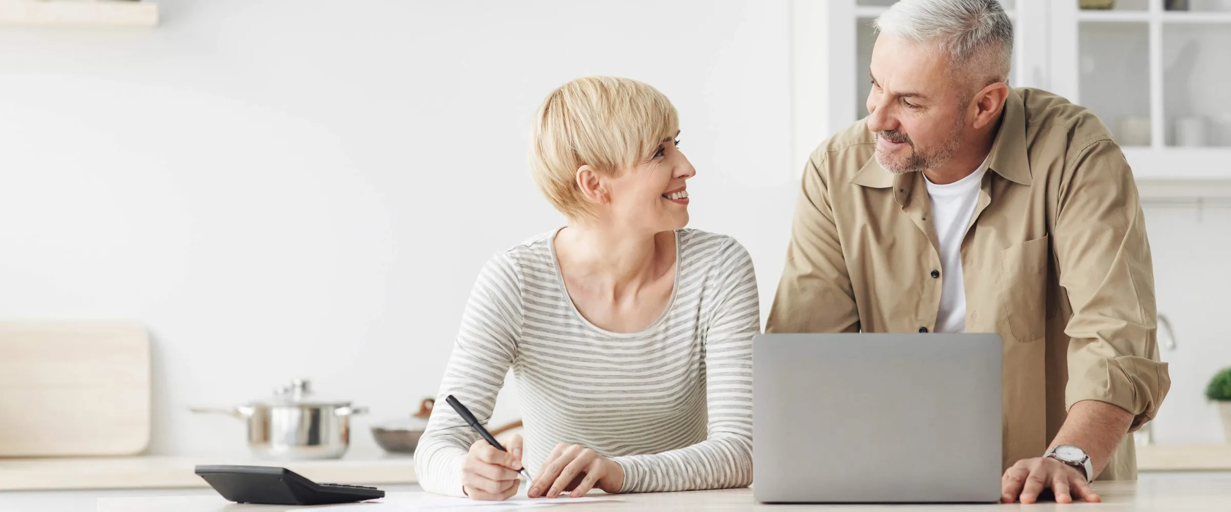 two people sitting down with a laptop, one is holding a pen smiling at the other