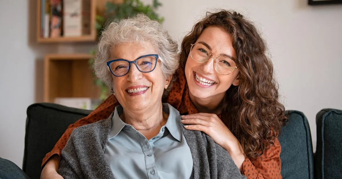 Portrait of grandma and adult granddaughter hugging on sofa