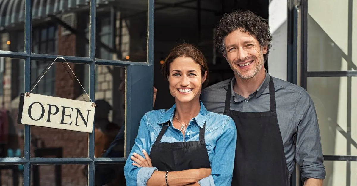 Male and female business owners standing in front of a door with an open sign.