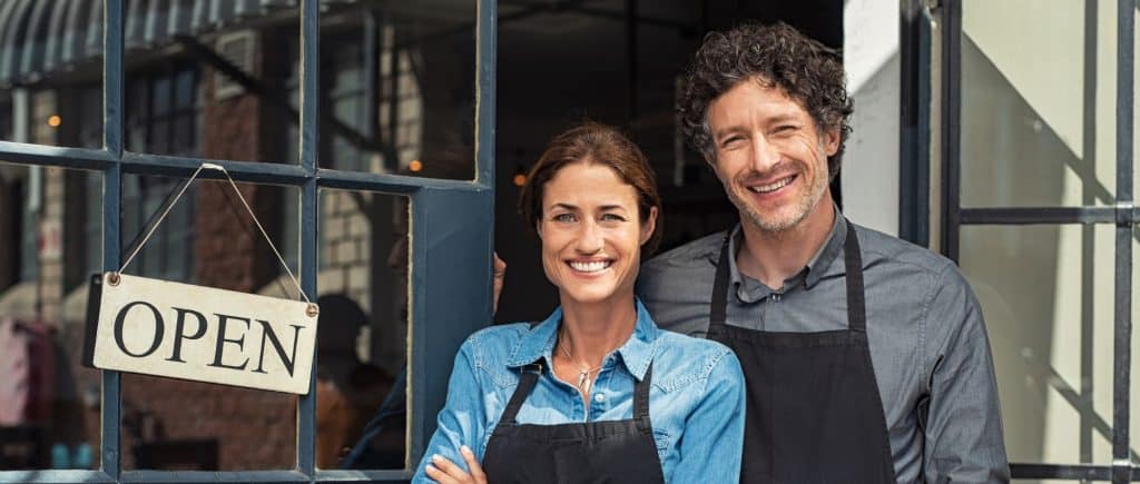 Male and female business owners standing in front of a door with an open sign.