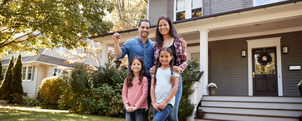 Family standing in front of their new home with keys