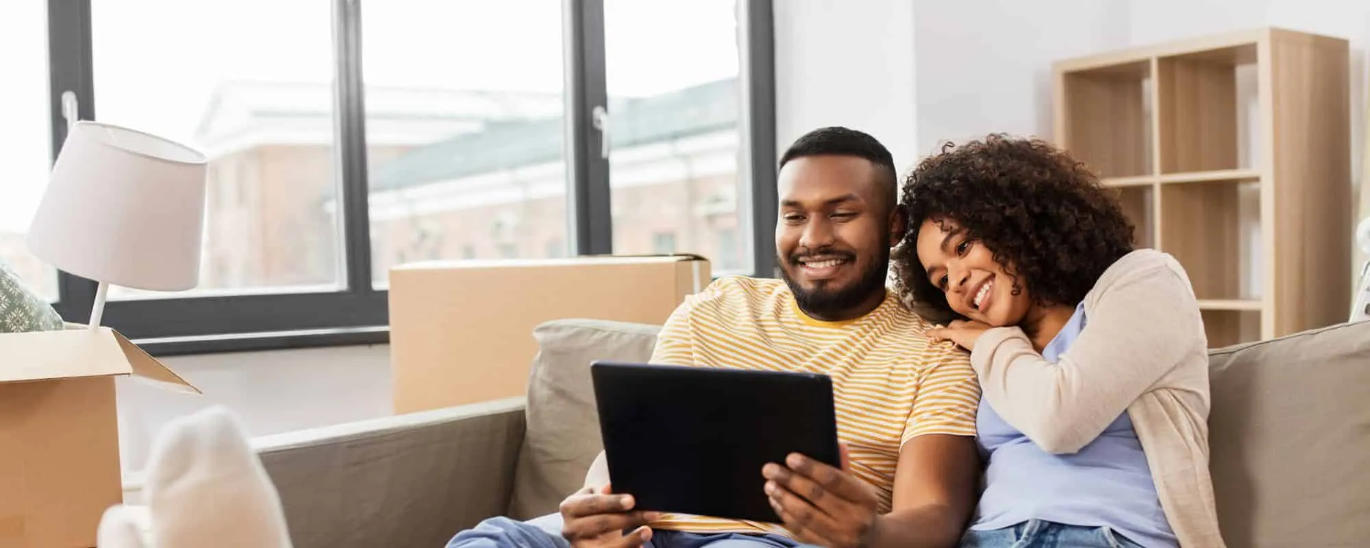 A couple sitting on a couch in their new home looking at a tablet