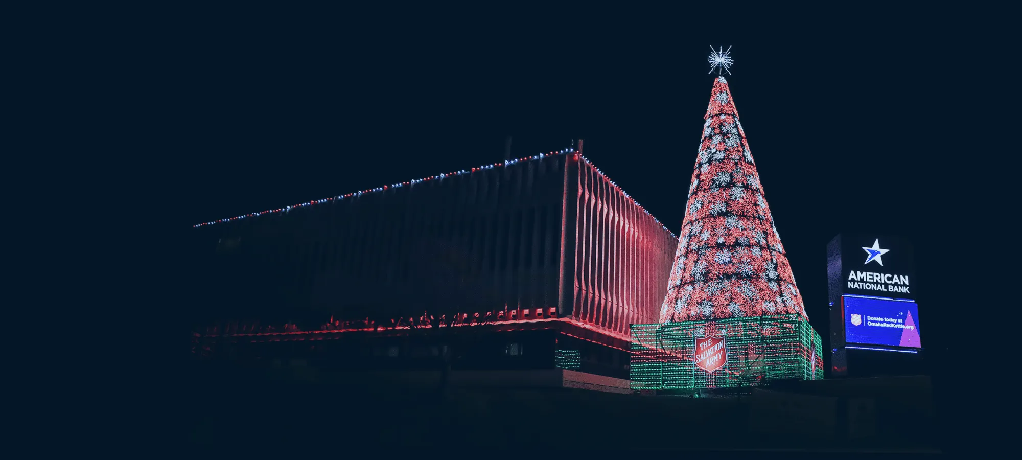 American National Bank building with red holiday lights next to an LED Christmas tree and the American National Bank marquee.