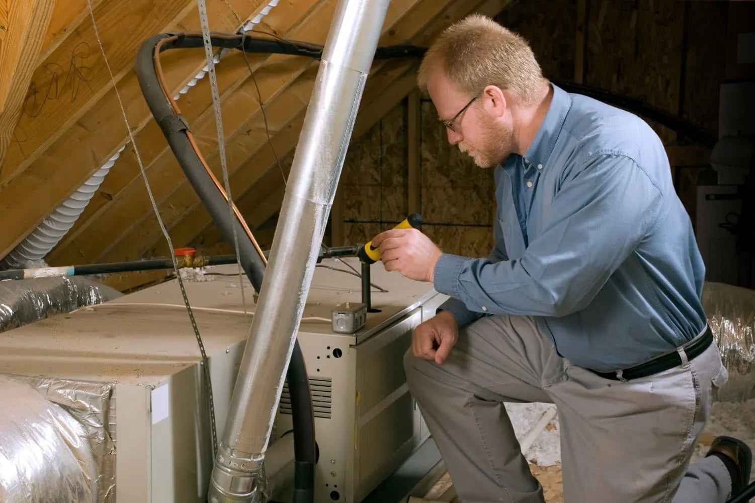 A person working on an air conditioner in an attic